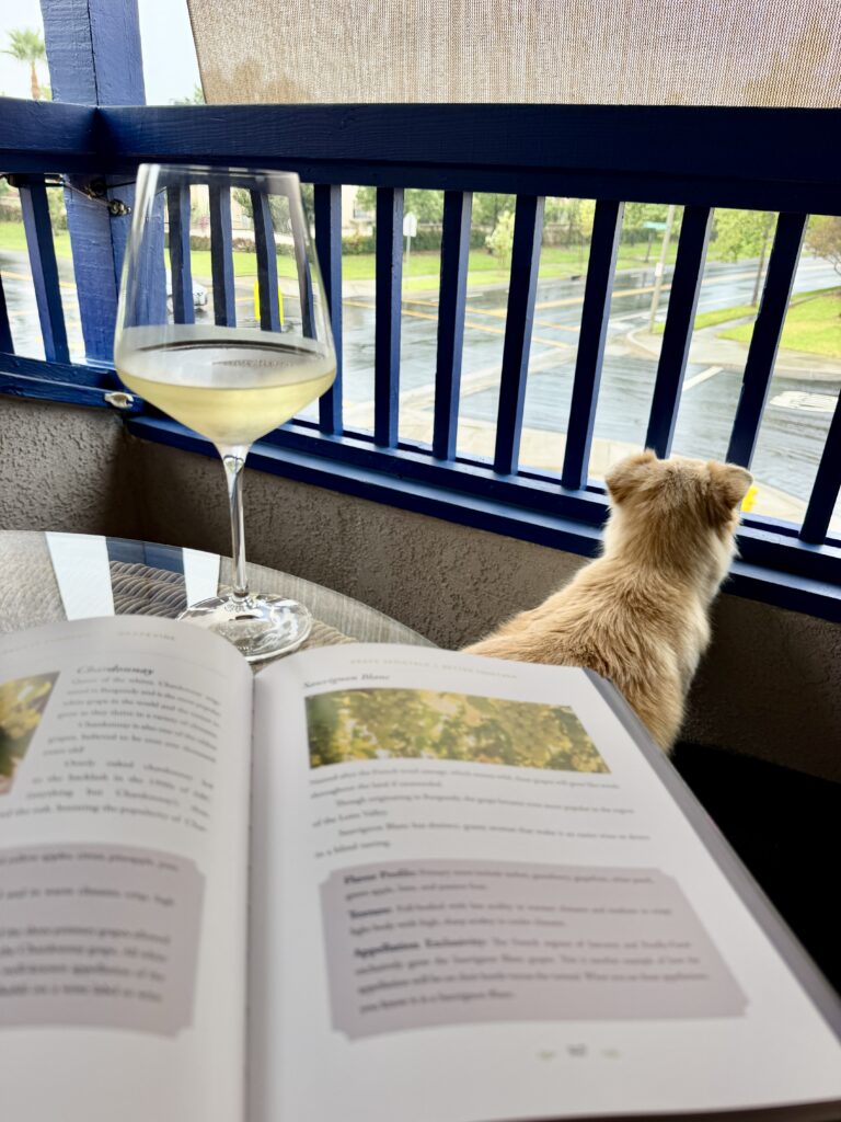 dogs and a glass of wine by a table with the wine book review subject on the table, I Learned It Through the Grapevine